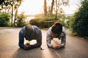 Athletes doing plank exercise on road in park during sunset