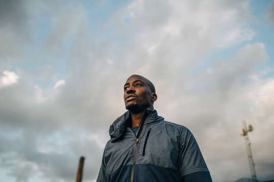 Thoughtful male athlete standing against cloudy sky