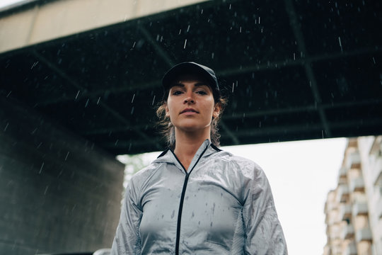 Portrait of female athlete standing against bridge during rainy season