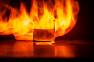 Whiskey in fire concept. Glass of whiskey and ice on wooden surface with color light and fog on background. Close up.