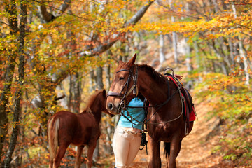 Woman near the horse and foal in the autumn forest