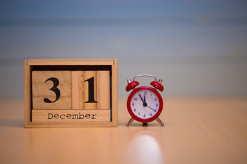 December 31st on wooden calendar and red alarm clock with blue background