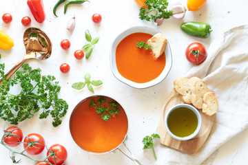 Gazpacho soup in metal pan and plate with fresh tomatoes, green sauce, chili, garlic, Basil and French baguette on white background. Top view