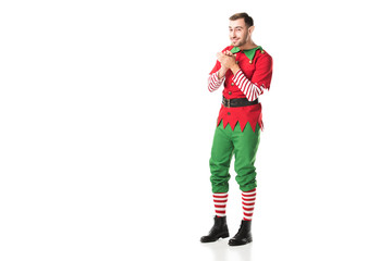 excited smiling man in christmas elf costume looking at camera and rubbing hands in anticipation isolated on white