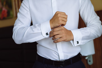 Closeup businessman puts on cufflinks, wears expensive leather belt. Man in a business suit, white...