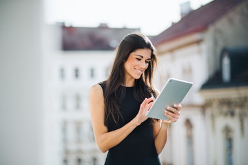 Fototapeta premium Young businesswoman with tablet standing on a terrace outside an office in city.