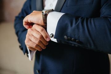 Closeup businessman puts on cufflinks and wristwatches, wears expensive leather belt. Man in a...