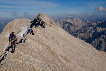 Mann klettern am Berggrat mit Blick auf rote Hütte, Jubiläumsgrat in Bayern