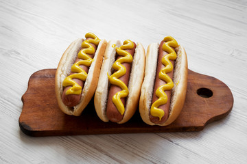 Hot dog with yellow mustard on wooden board on white wooden table, side view. Close-up.