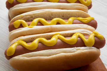 Hot dog with yellow mustard on wooden board on white wooden background, side view. Close-up.