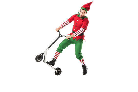 excited man in christmas elf costume jumping in air on push-cycle isolated on white