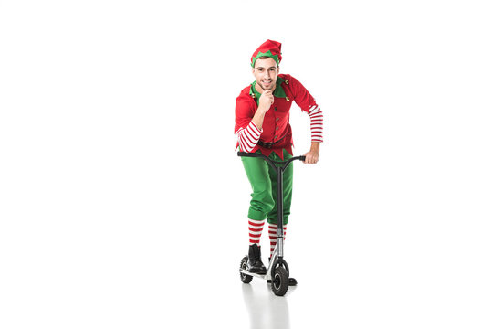 happy man in christmas elf costume touching chin and riding push-cycle isolated on white