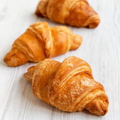 Fresh croissants on white wooden table, side view. Selective focus.