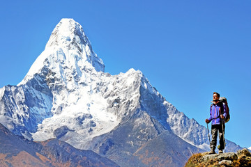 Tourist with backpack reaches the summit of mountain peak. Beautiful view of Ama Dablam on a trek to Everest base camp. Success, freedom and happiness, achievement in mountains. Active sport concept. 