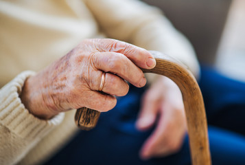 A close-up of a senior woman holding a walking stick at home.