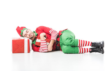 man in christmas elf costume sleeping on pile of presents isolated on white