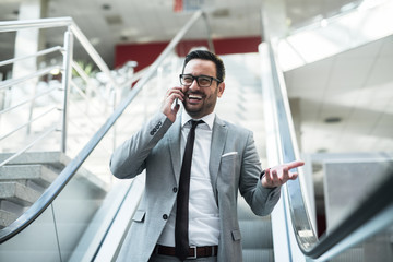 Businessman using smart phone for business talk while going down the escalator.