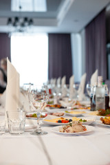 The served festive table is covered with a white tablecloth with dishes and drinks with glasses in the ceremonial hall