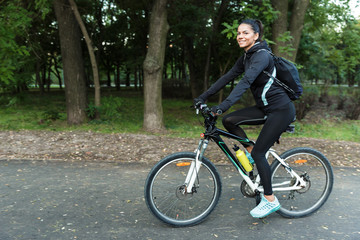 Beautiful woman walking on bicycle in the park outdoors.