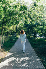 Fototapeta premium Young woman walking away on path in green park
