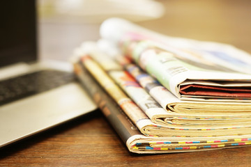 Newspapers and computer. Laptop and daily papers on the table. Fresh news by  paper or by electronic device, different ways of communication. Source of information, actual data on pages or on screen