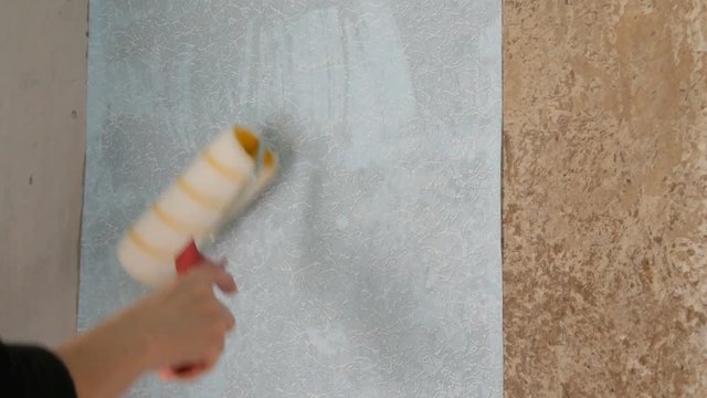 Sheet of blue papper wallpaper is glued to the wall with a special construction roller
