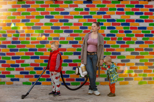 Happy village children and their slender mother with vacuum cleaner opposite the multi-colored brick wall. Romantic lighting with reflection of sunlight. Effect of lense flare without postproduction