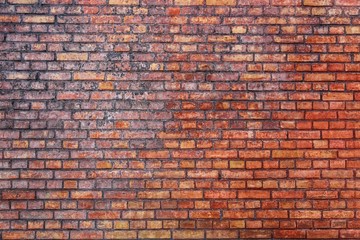 Old and weathered grungy red brick wall marked by the long exposure to the elements as surface texture background.