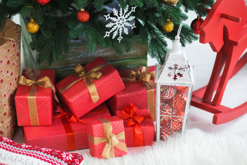 Christmas holiday decor. Red vintage wooden horse, many presents boxes in wrapping paper, lantern with ornaments and green tree. Horizontal color image.