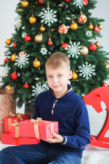 Portrait of white kid holding red christmas present in hands. Vertical color photography.