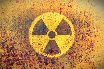 Round yellow radioactive (ionizing radiation) danger symbol painted on a massive rusty metal wall with rustic grunge texture background. Washed fading yellow rust color toned. - obrazy, fototapety, plakaty