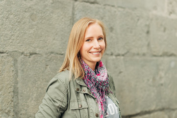 Outdoor portrait of beautiful blond woman, posing outdoors, wearing khaki color parka and pink scarf