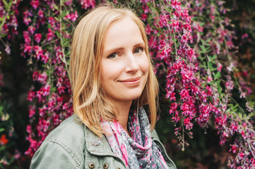 Outdoor portrait of beautiful blond woman, posing outdoors, wearing khaki color parka and pink scarf