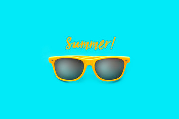 Summer! text and yellow sunglasses in intense cyan blue large negative space background. Minimal image concept for ready for summer, sun protection, hot days and tropical travel vacation.