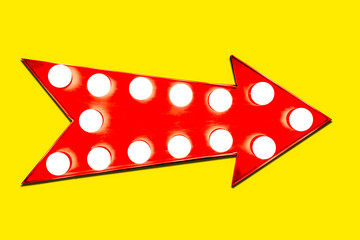 Red arrow shaped vintage colorful illuminated metallic display direction sign with glowing light bulbs on an intense vivid yellow background.