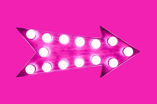 Pink arrow shaped vintage colorful illuminated metallic display direction sign with glowing light bulbs isolated on an intense same color bright vivid pink background.