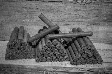 Cigars lie stacked on a wooden table in several blocks. View in black and white. Concept: cigars or health or livestyle
