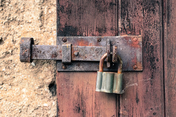 Closed old rusty iron lock and vintage padlock on cracking and peeling weathered red wooden door.