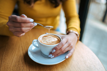 Female hands holding cup of coffee and spoon with foam.