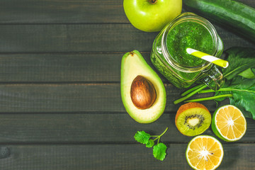 healthy green smoothie with ingredients on a wooden table: apple, kiwi, lime, spinach, mint, avocado, cucumber