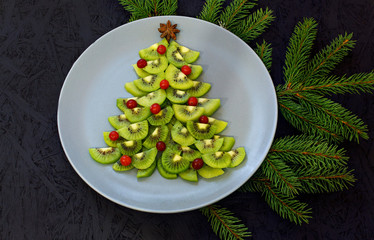 Kiwi slices laid out on a plate in the shape of a Christmas tree on a black background. View from above. New Year and Christmas