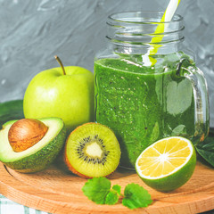 healthy green smoothie with ingredients on a wooden table: apple, kiwi, lime, spinach, mint, avocado, cucumber