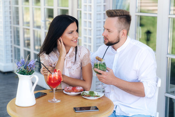 Man and a woman are sitting in a cafe, looking at each other lovingly, eating delicious desserts and drinking cocktails. A man wants to make an offer today to marry a beautiful girl.