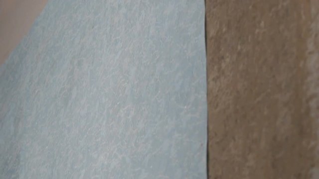 Close up sheet of blue papper wallpaper is glued to the wall with a special construction roller