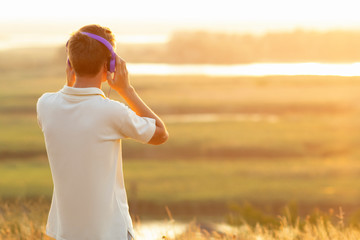 teenager in headphones listening to music at sunset in the field