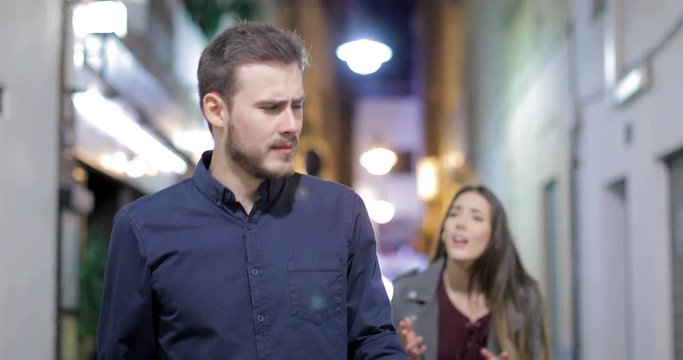 Front view of a unhappy couple breaking up arguing in the street in the night