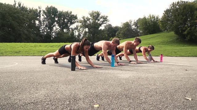 group of well-trained men and women doing elbow push ups, outdoor in the morning