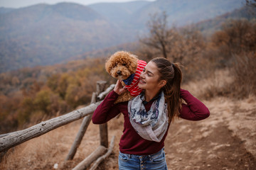 Woman holding her dog on shoulders outdoors.