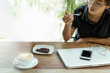 Young asian woman having coffee break with brownie cake in cafe selected focus.