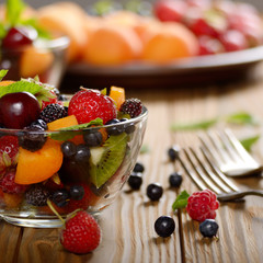 Assorted fruits in glass bowl on kitchen wooden table with fork aside